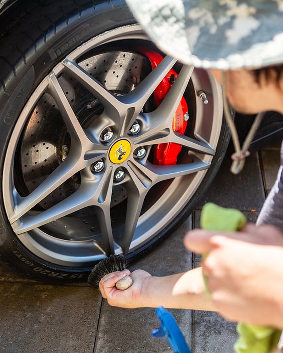 Hand cleaning a Ferrari wheel and its red caliper
